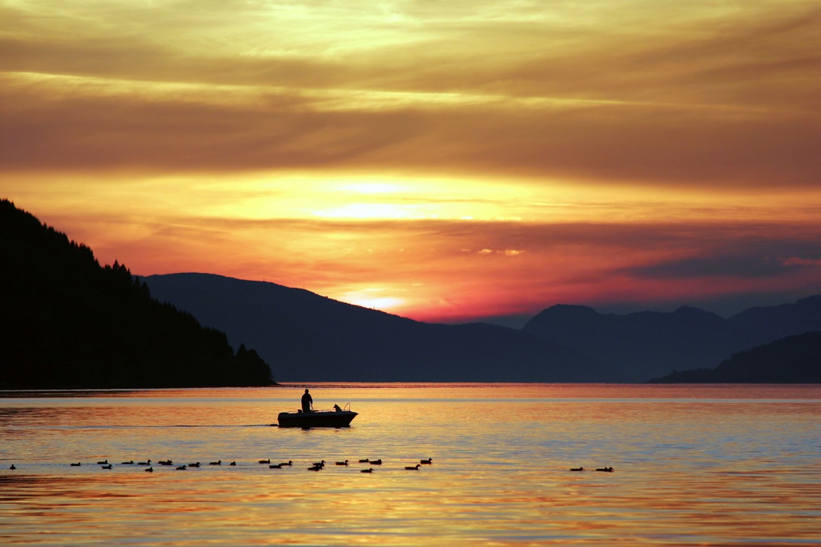 A small boat crossing calm water at golden sunset beneath dark coastal mountains (placeholder photo)