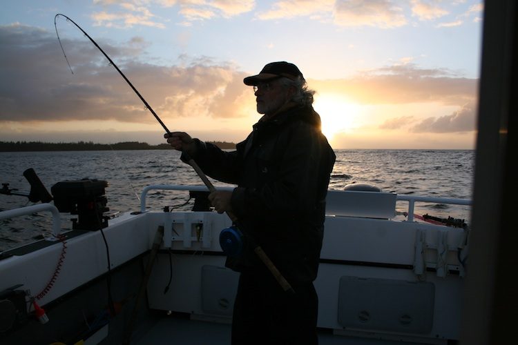 An angler silhouetted against the sunset, playing a fish from the deck of a charter boat (placeholder photo)